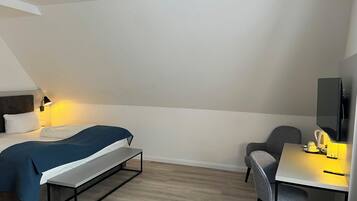 A hotel room with a bed, a desk, a chair, a TV, and a bedside table.