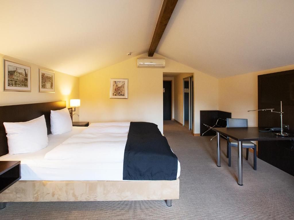 Una habitación de hotel con cama, mesita de noche, lámpara, escritorio y silla.