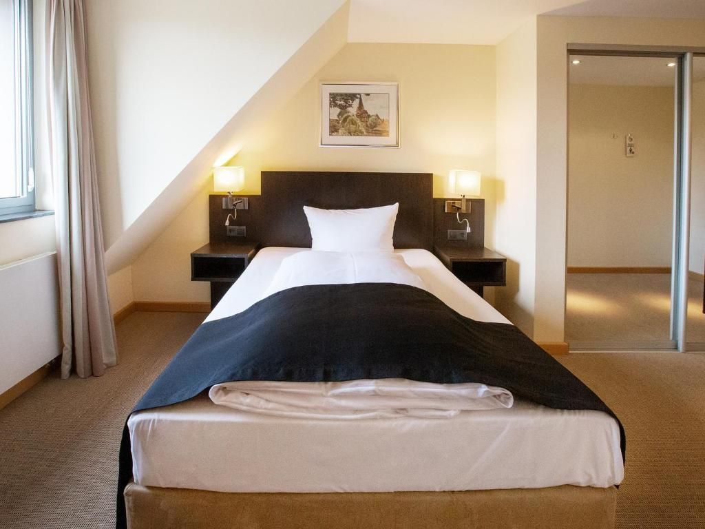A hotel room with a bed, two bedside tables with lamps, a framed picture on the wall, and a door leading to another room.