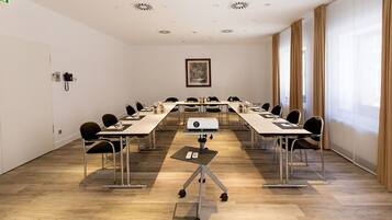 A conference room with a long table, chairs, a projector, and a small table with a laptop.