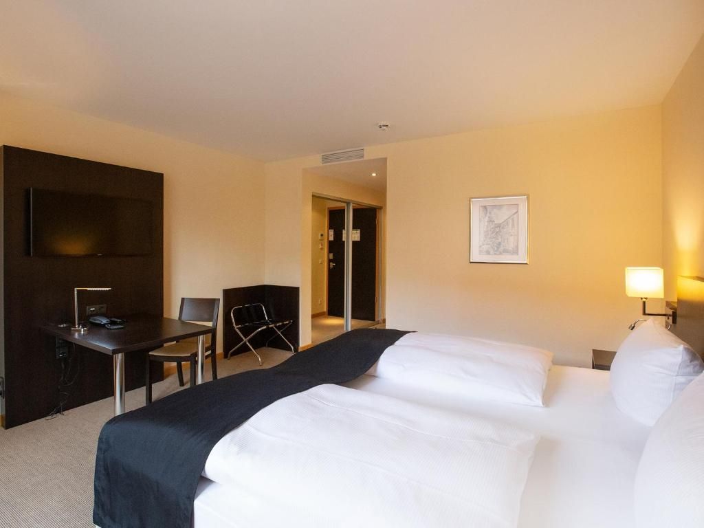 A hotel room with a bed, a desk, a chair, and a television.
