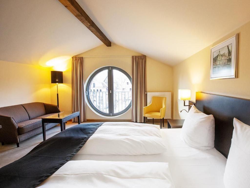 A hotel room with a large bed, a sofa, a chair, a desk, and a window with curtains.