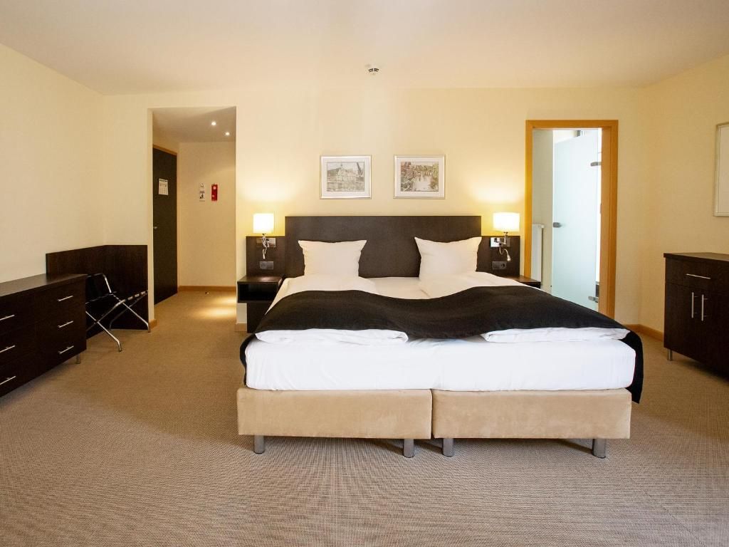 Quarto de hotel com uma cama grande, mesas de cabeceira, um guarda-roupa e uma porta que dá para outro espaço.