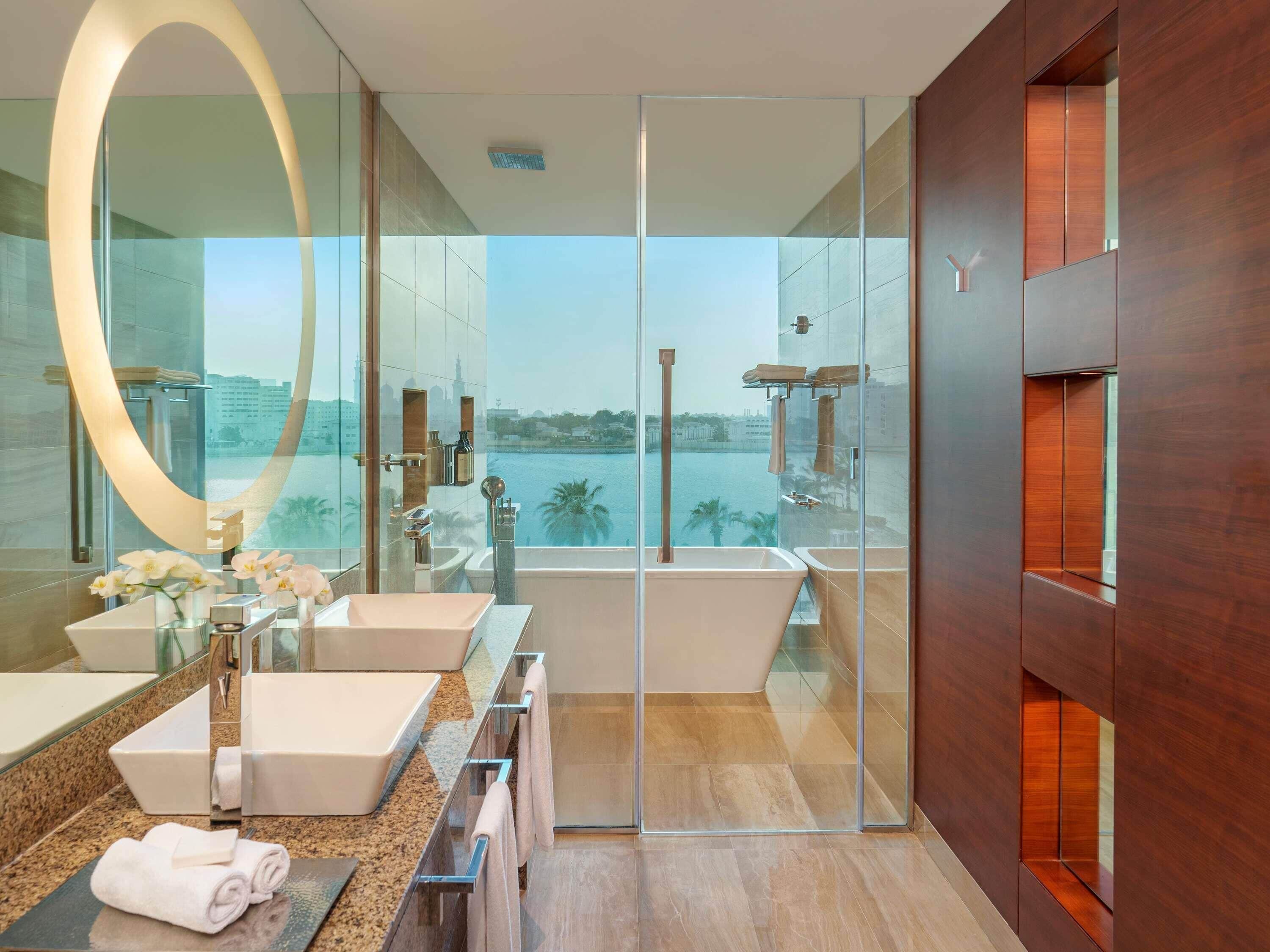 Un baño moderno con un espejo grande, dos lavamanos, una bañera y una ducha con cerramiento de vidrio.