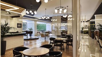 Relax in a stylish space with round tables, chairs, and a piano, surrounded by lush greenery and modern lighting.