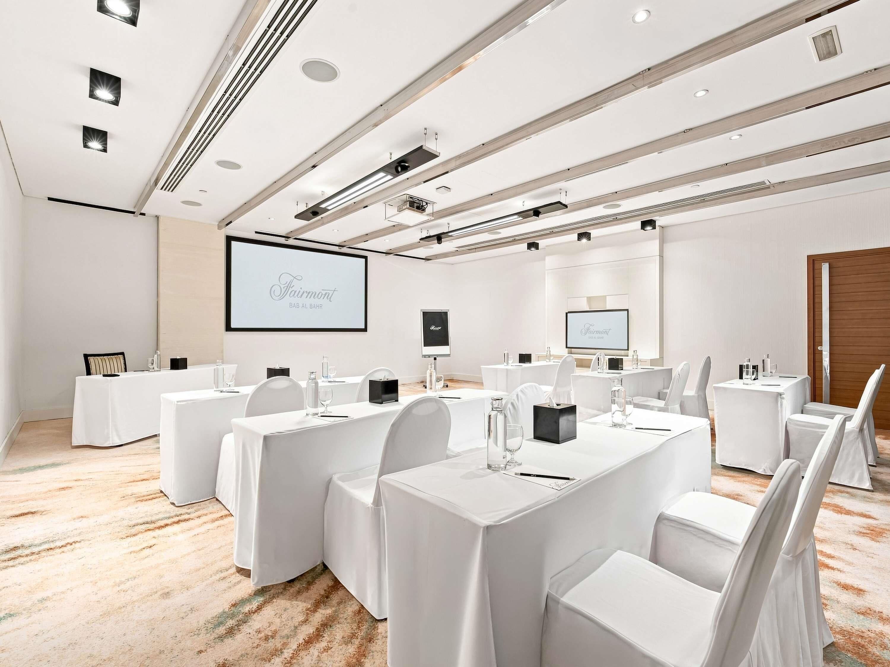 A conference room with multiple tables, chairs, a large screen, and a wooden door.