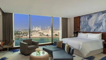 A hotel room with a large bed, a sofa, a coffee table, and a view of a city skyline.