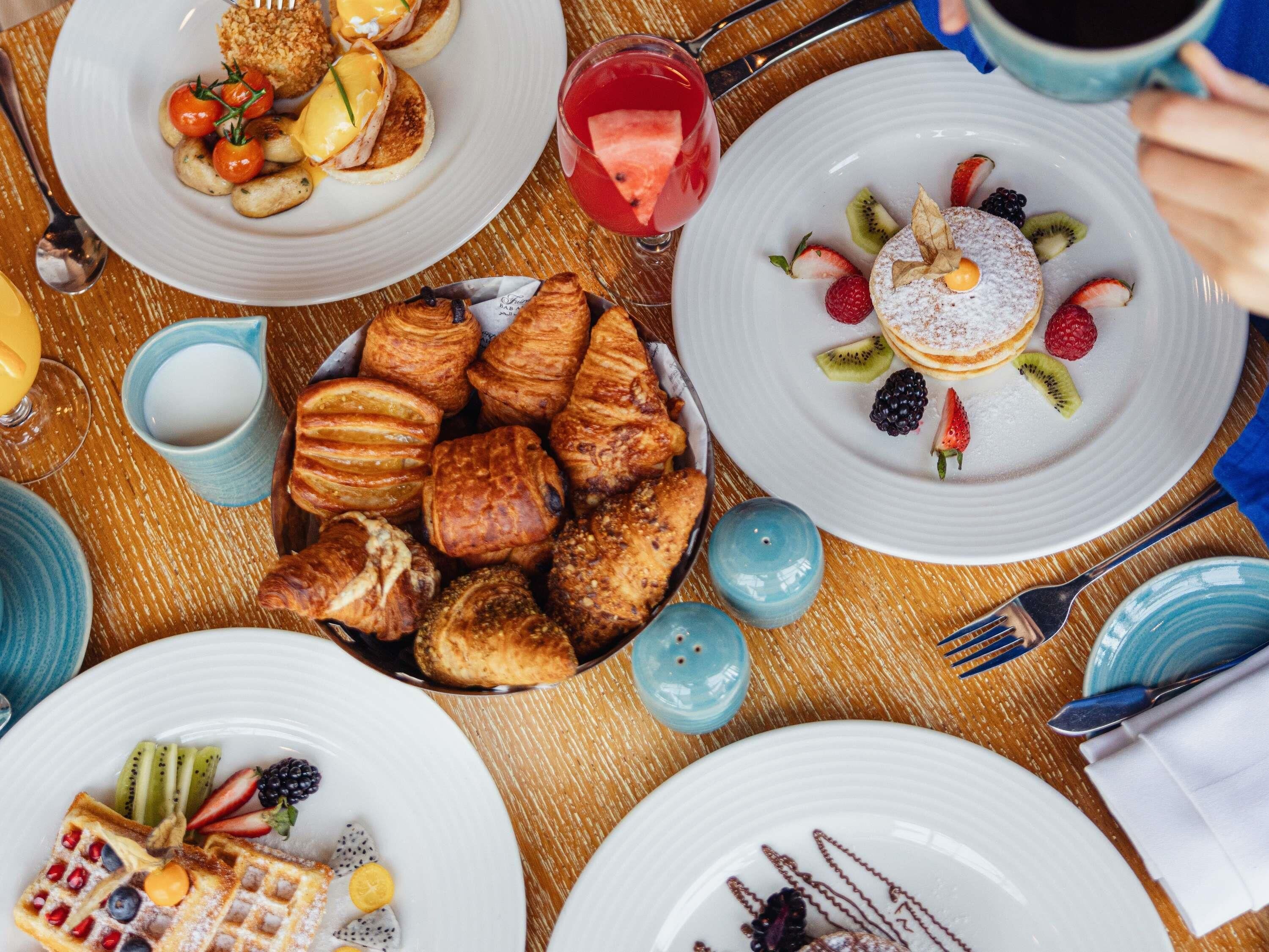 A breakfast setting with various dishes including pancakes, waffles, croissants, and fruit.