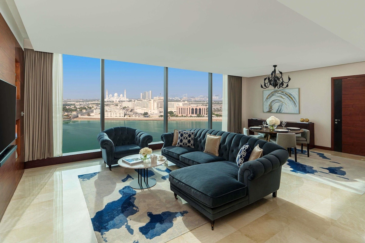 A modern living room with a large window, a sofa set, a coffee table, and a dining area.