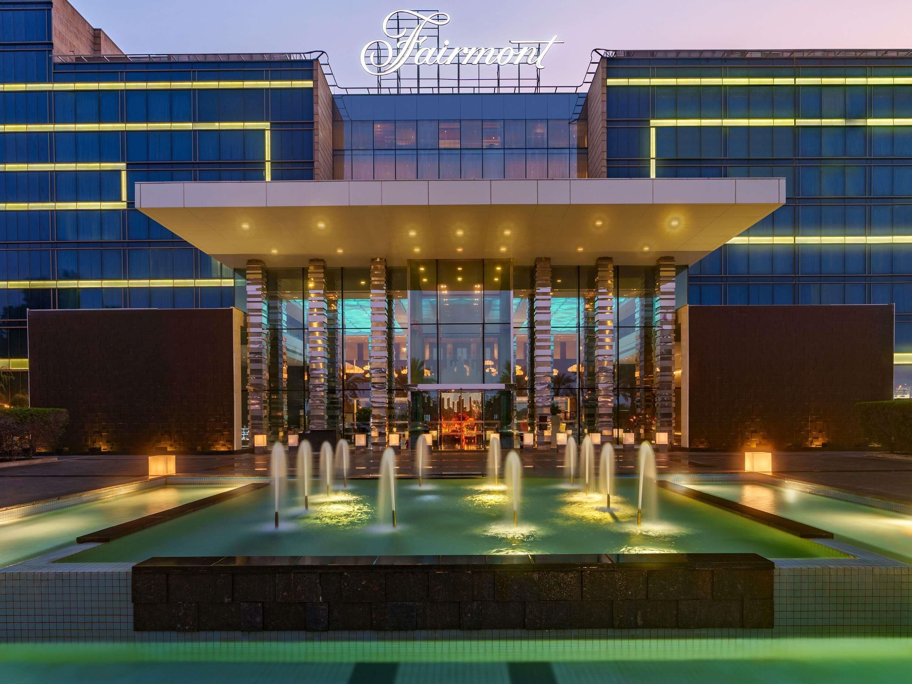 A hotel with a modern facade, a central entrance with a covered area, and a water feature in front.