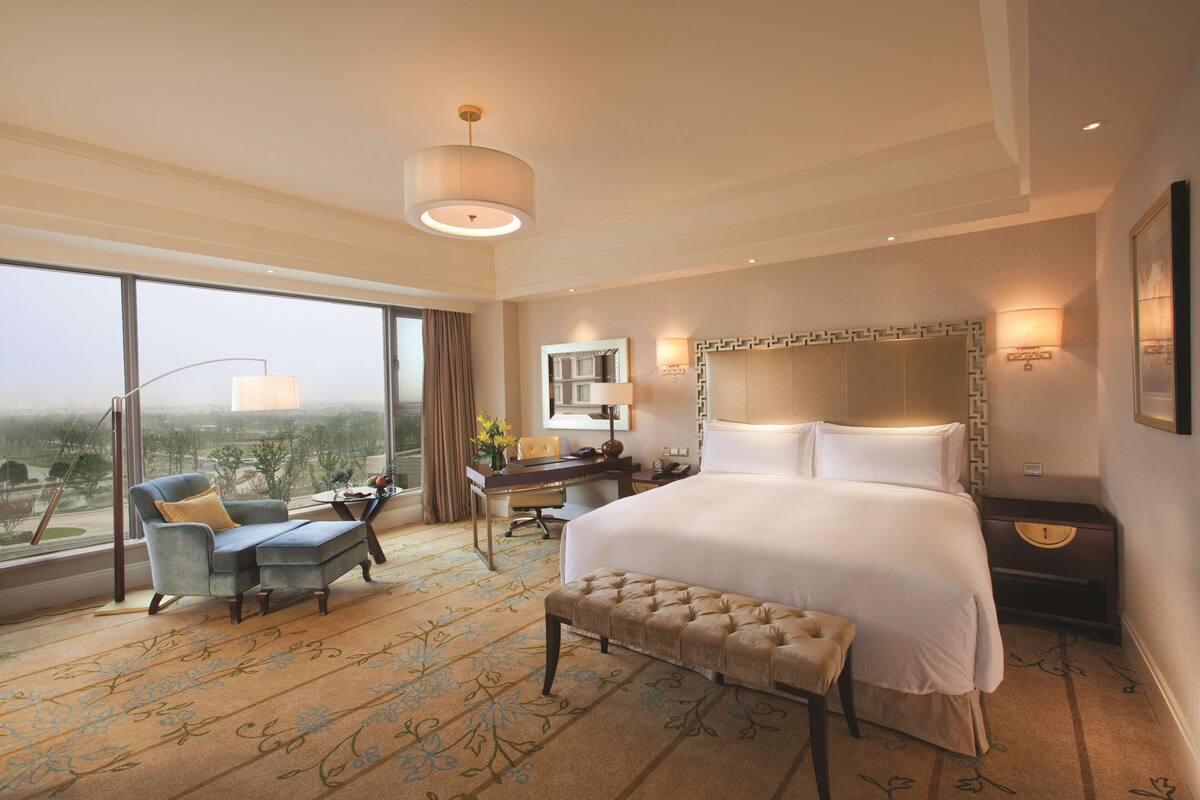 A spacious hotel room with a large bed, a desk with a chair, a sofa, and a view of the city.