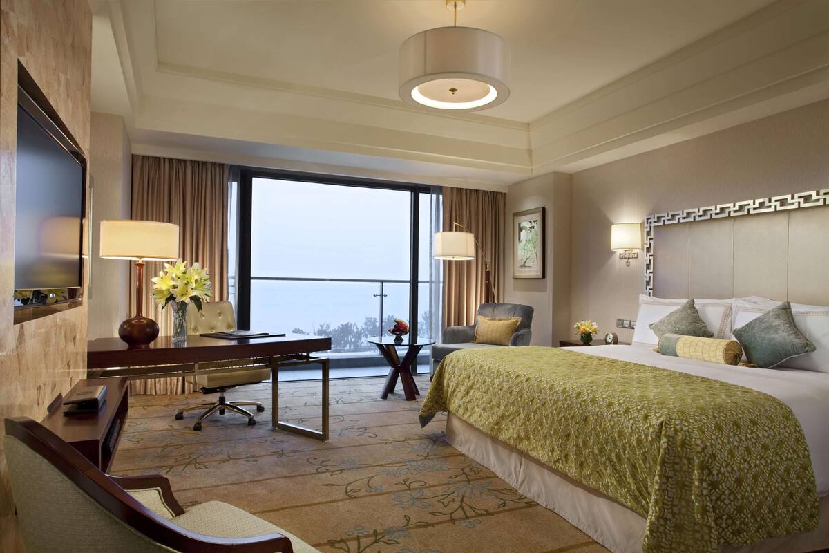 A hotel room with a large bed, a desk with a chair, a TV, and a balcony with a view.