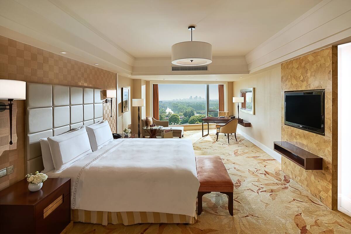A hotel room with a large bed, a desk, a chair, a television, and a view of the city.