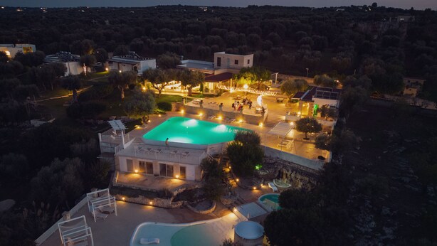 An aerial view of a resort with a central swimming pool, multiple outdoor seating areas, and a well-lit building complex. - Hotel Resort Corte Di Ferro (Carovigno)