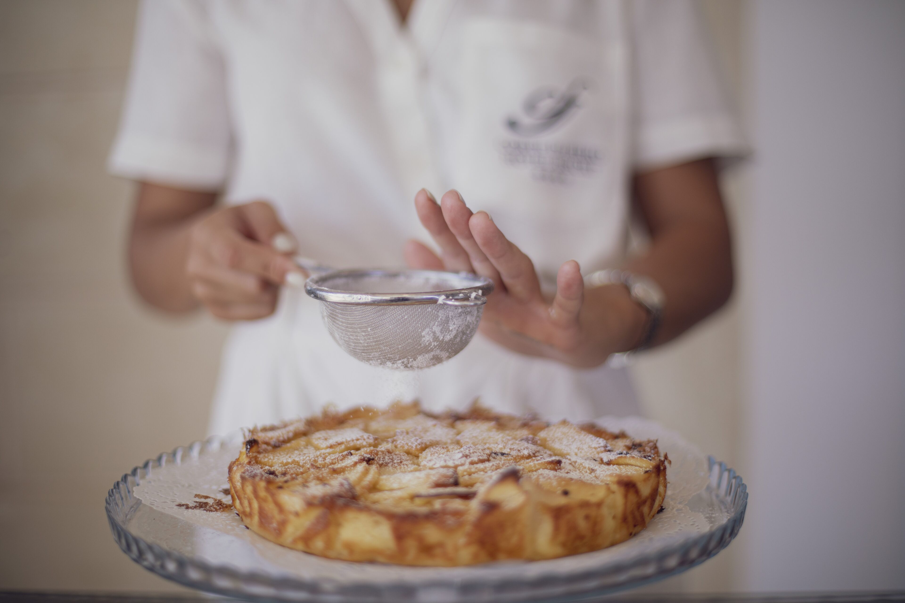 A person holding a sieve above a pie on a plate.