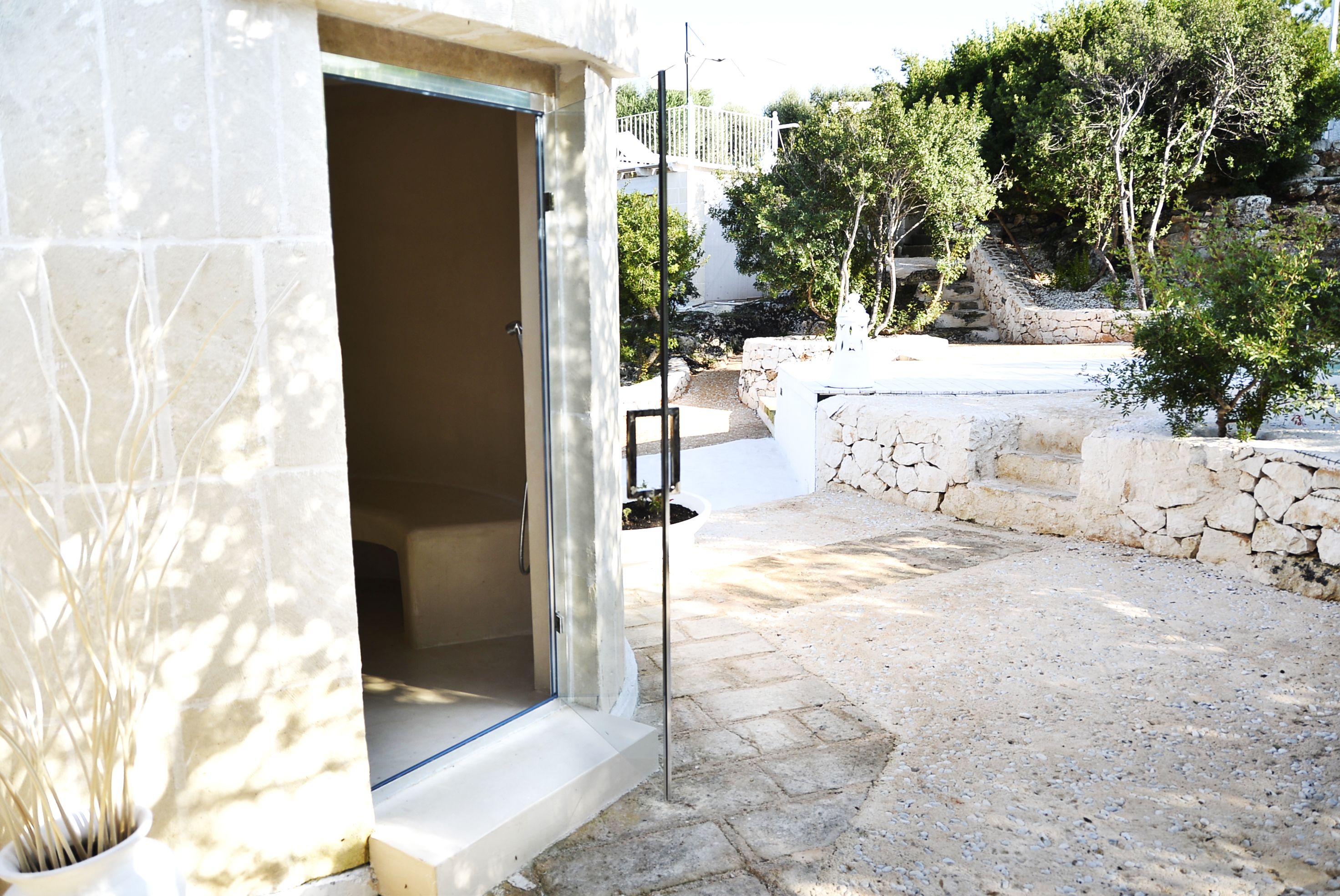 Un sendero de piedra que conduce a un edificio con una puerta abierta, rodeado de árboles y un muro de piedra.