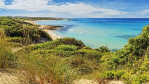 A coastal landscape with a beach, clear blue water, and green vegetation. - Hotel Resort Corte Di Ferro (Carovigno)