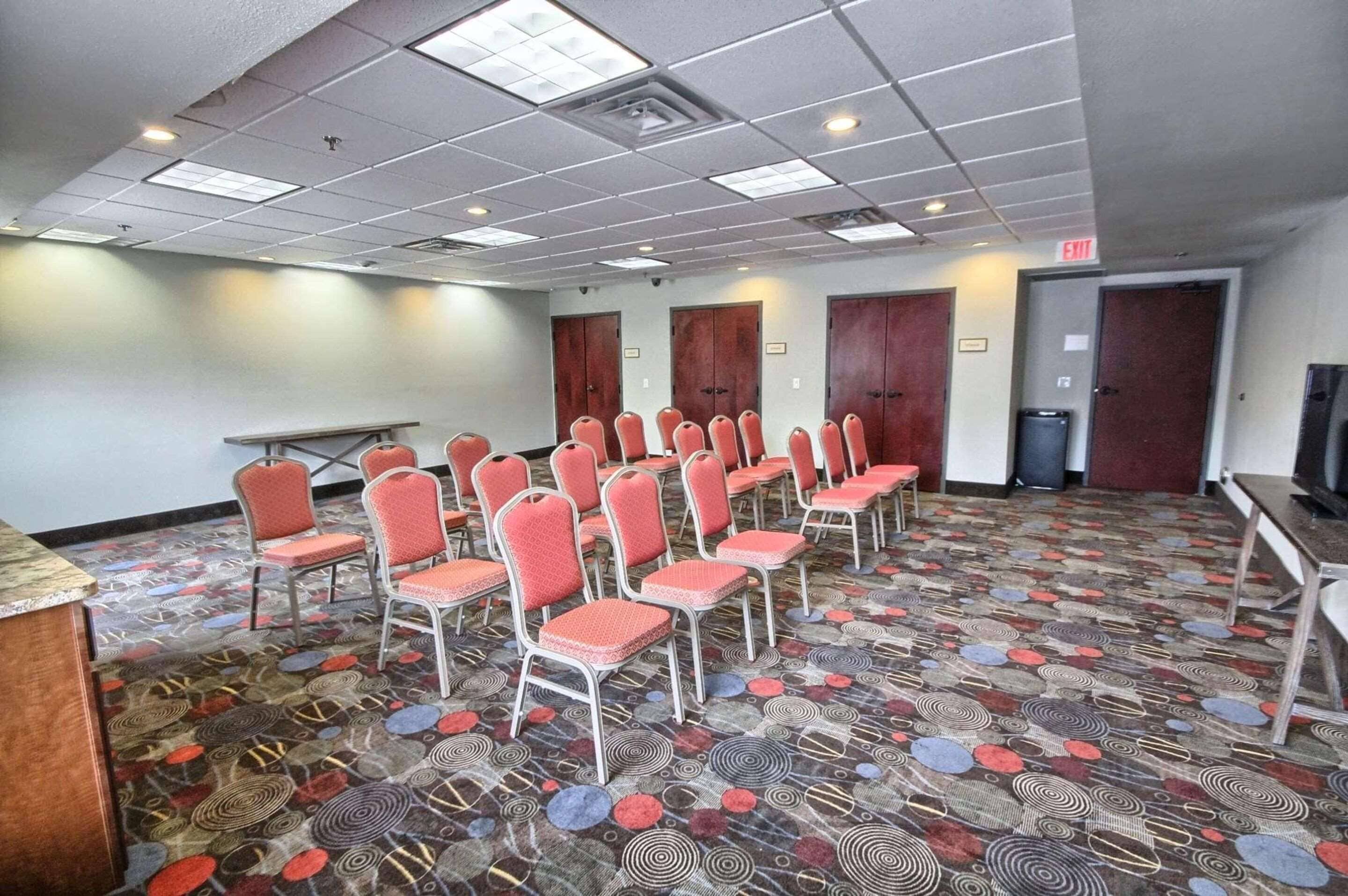A conference room with rows of chairs, a long table, and patterned carpet.