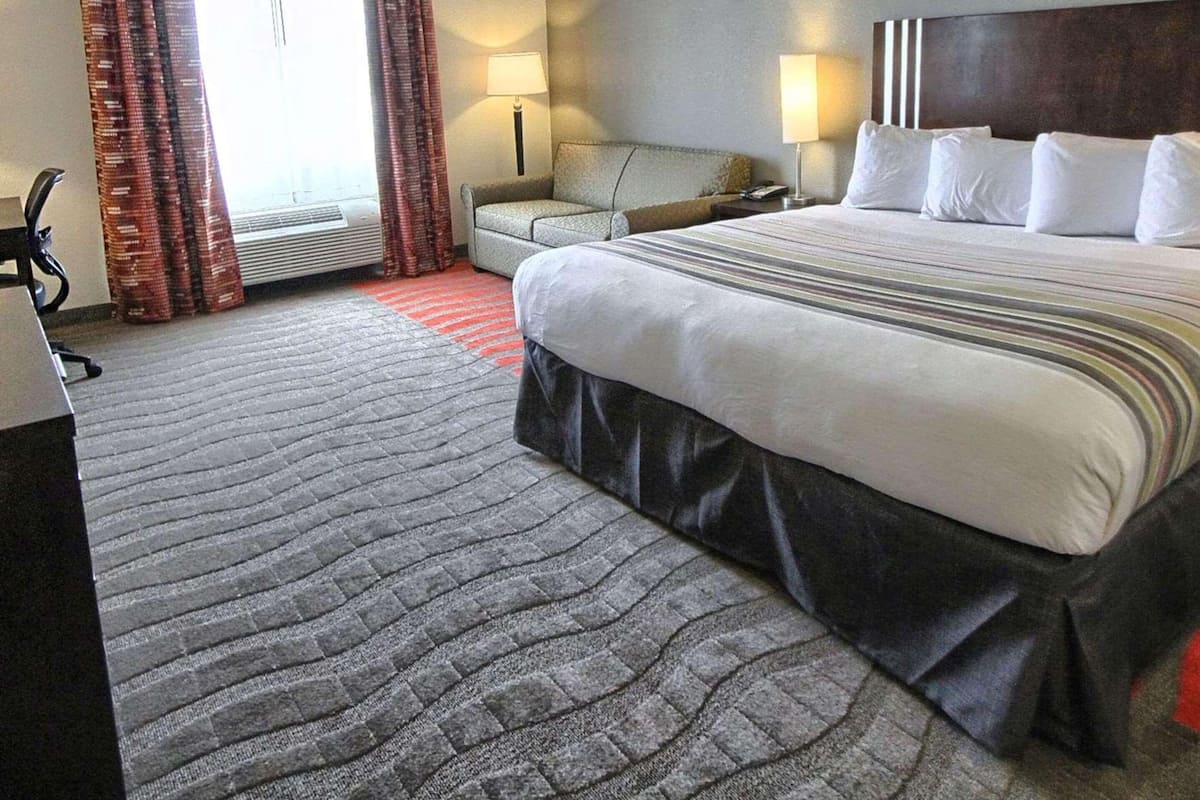 Une chambre d’hôtel avec un grand lit, un bureau, une chaise, une lampe et une fenêtre avec des rideaux.