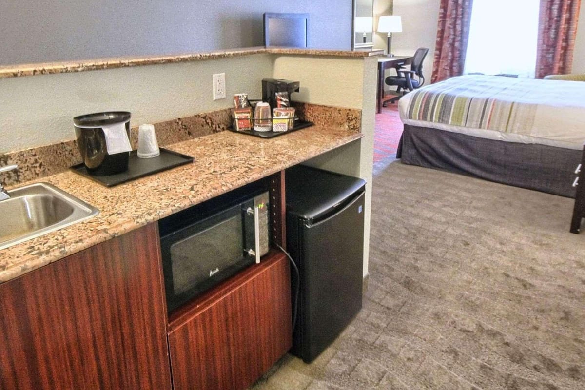 Une chambre d’hôtel équipée d’une kitchenette, d’un lit, d’un bureau et d’une fenêtre avec des rideaux.