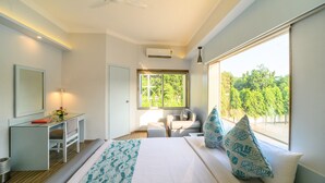 A modern bedroom with a bed, a desk, a chair, and a window with a view of trees. - Sinclairs Siliguri (Siliguri)