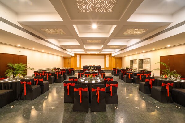 Une grande salle de banquet avec des tables rondes et des chaises noires ornées de rubans rouges, disposées en rangées.