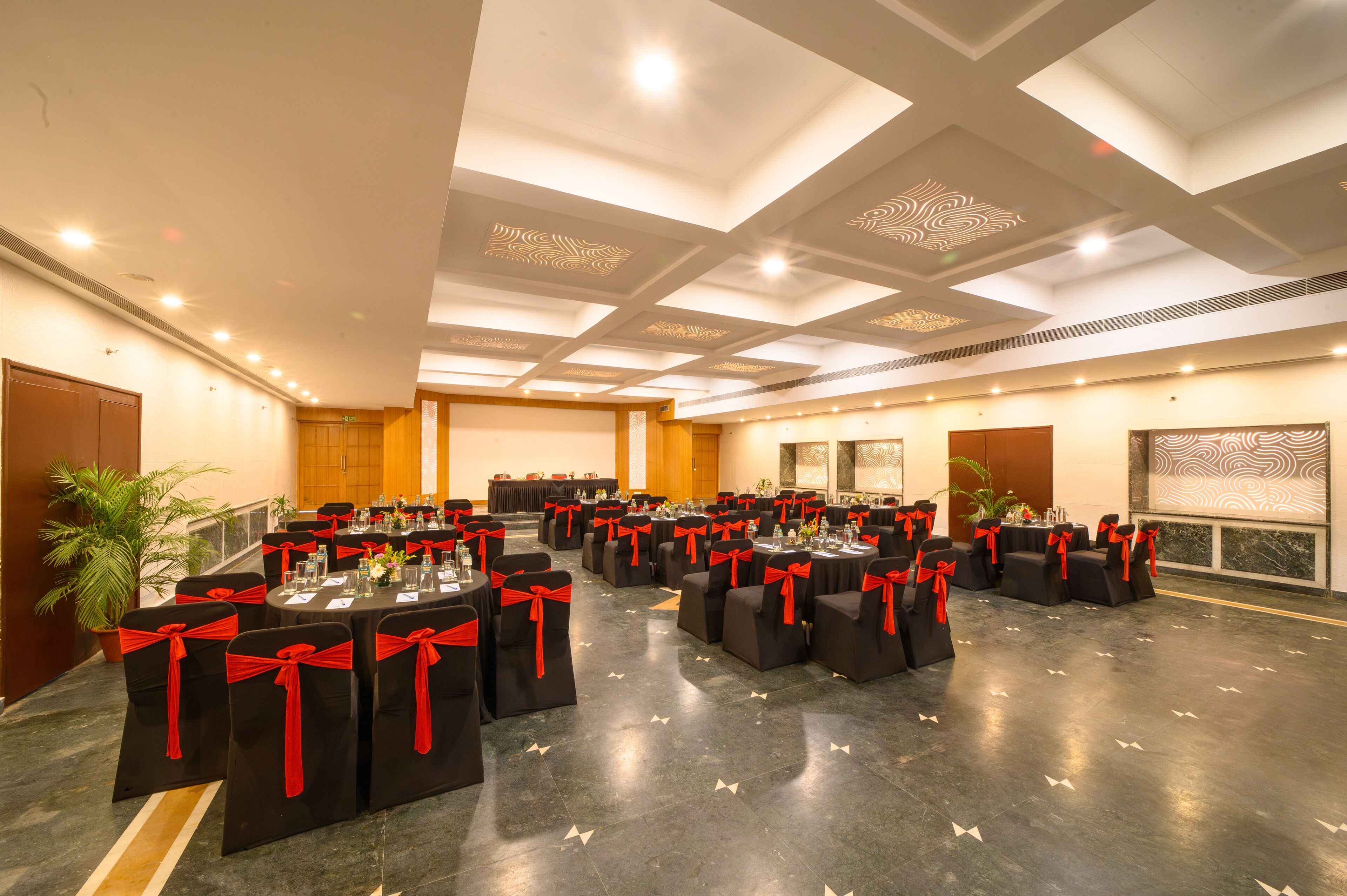 Un salón de conferencias con mesas y sillas, cada una adornada con cintas rojas, dispuesto para una reunión.