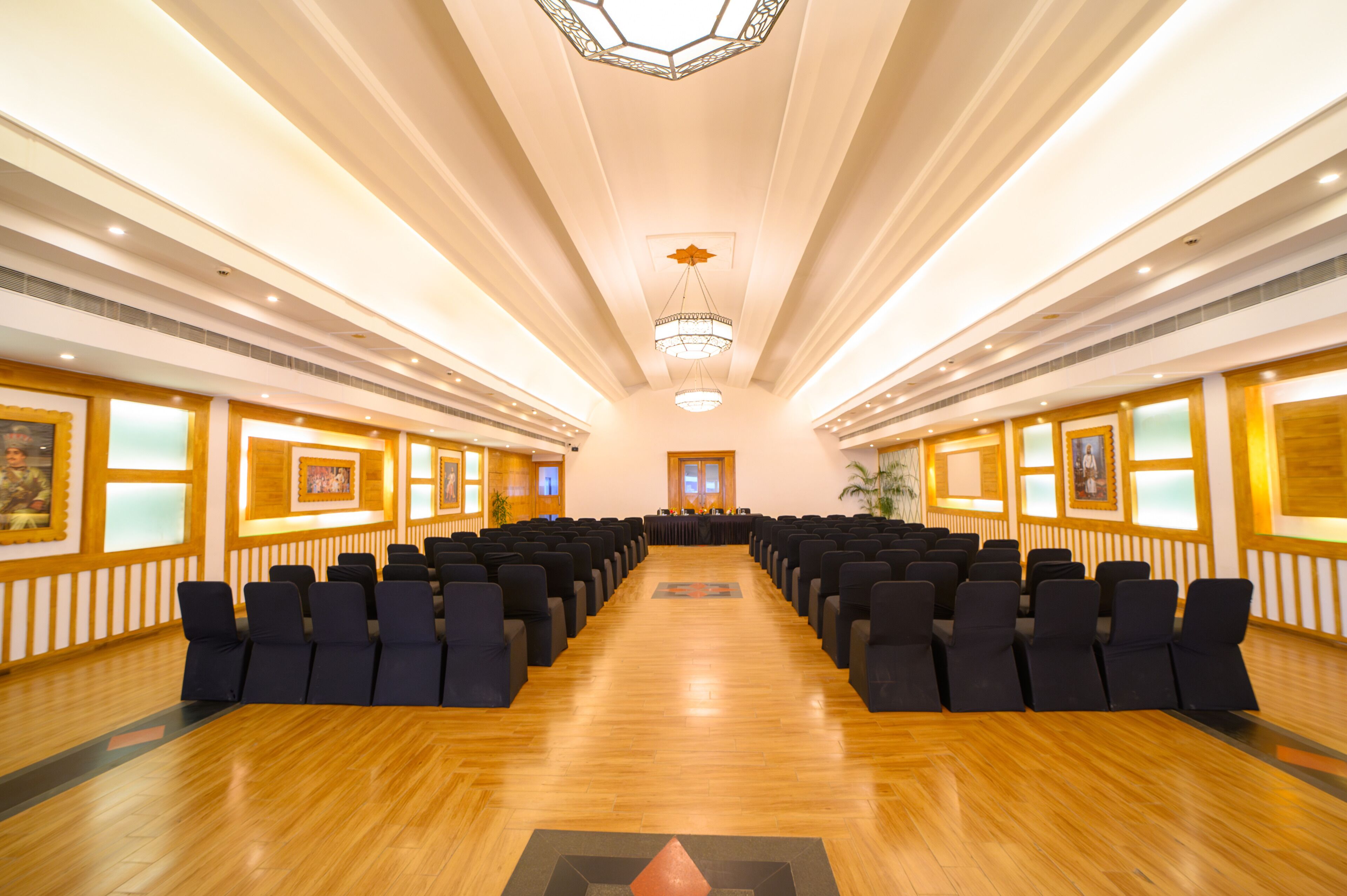 A conference room with rows of chairs facing a long table, wooden floors, and framed artwork on the walls.
