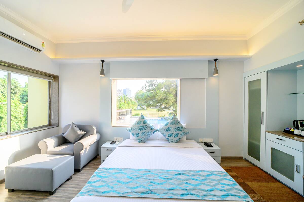 A modern hotel room with a large bed, a sofa, a desk, and a view of the outdoors.