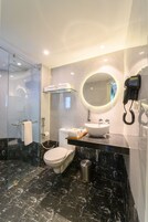 Un baño moderno con ducha de vidrio, inodoro blanco, lavamanos con espejo y secador de pelo en la pared.