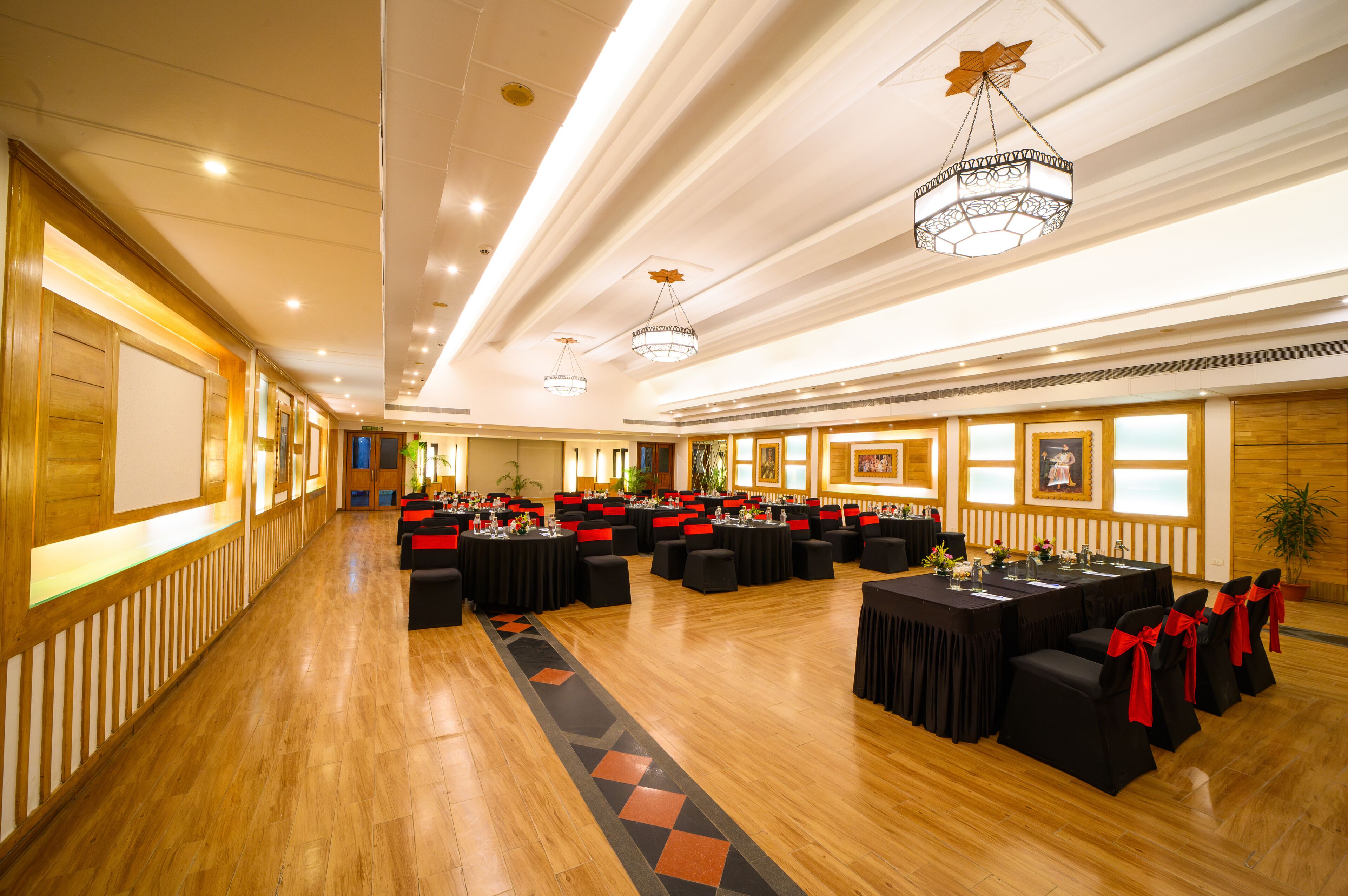 A spacious banquet hall with multiple round tables, black tablecloths, and red sashes.