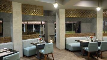 Un restaurant moderne avec un intérieur à la fois élégant et chaleureux, caractérisé par de hauts plafonds, des murs en briques apparentes et une variété de types de sièges, notamment des banquettes et des tables.