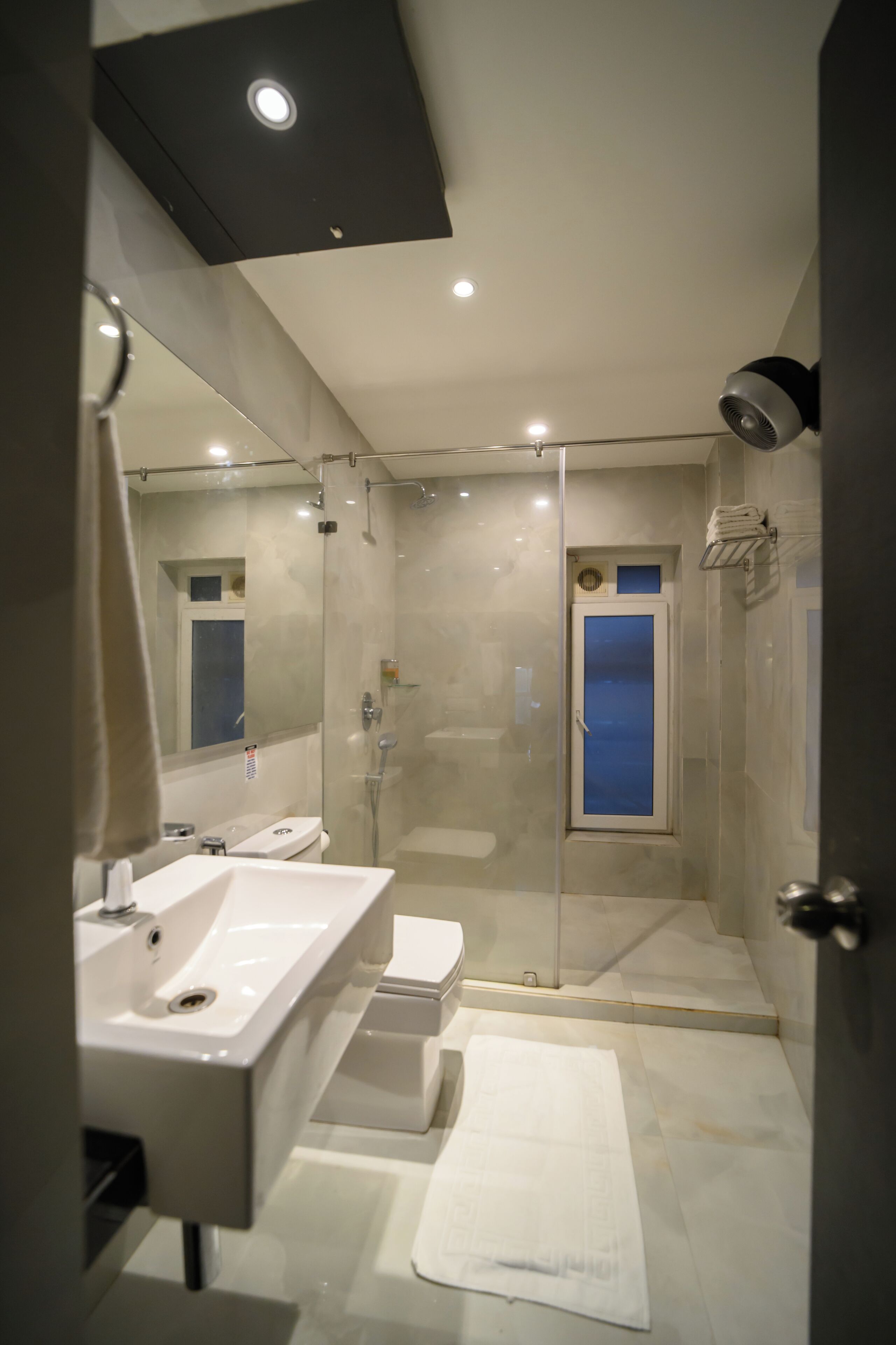 A modern bathroom with a glass-enclosed shower, a large mirror, and a white sink.