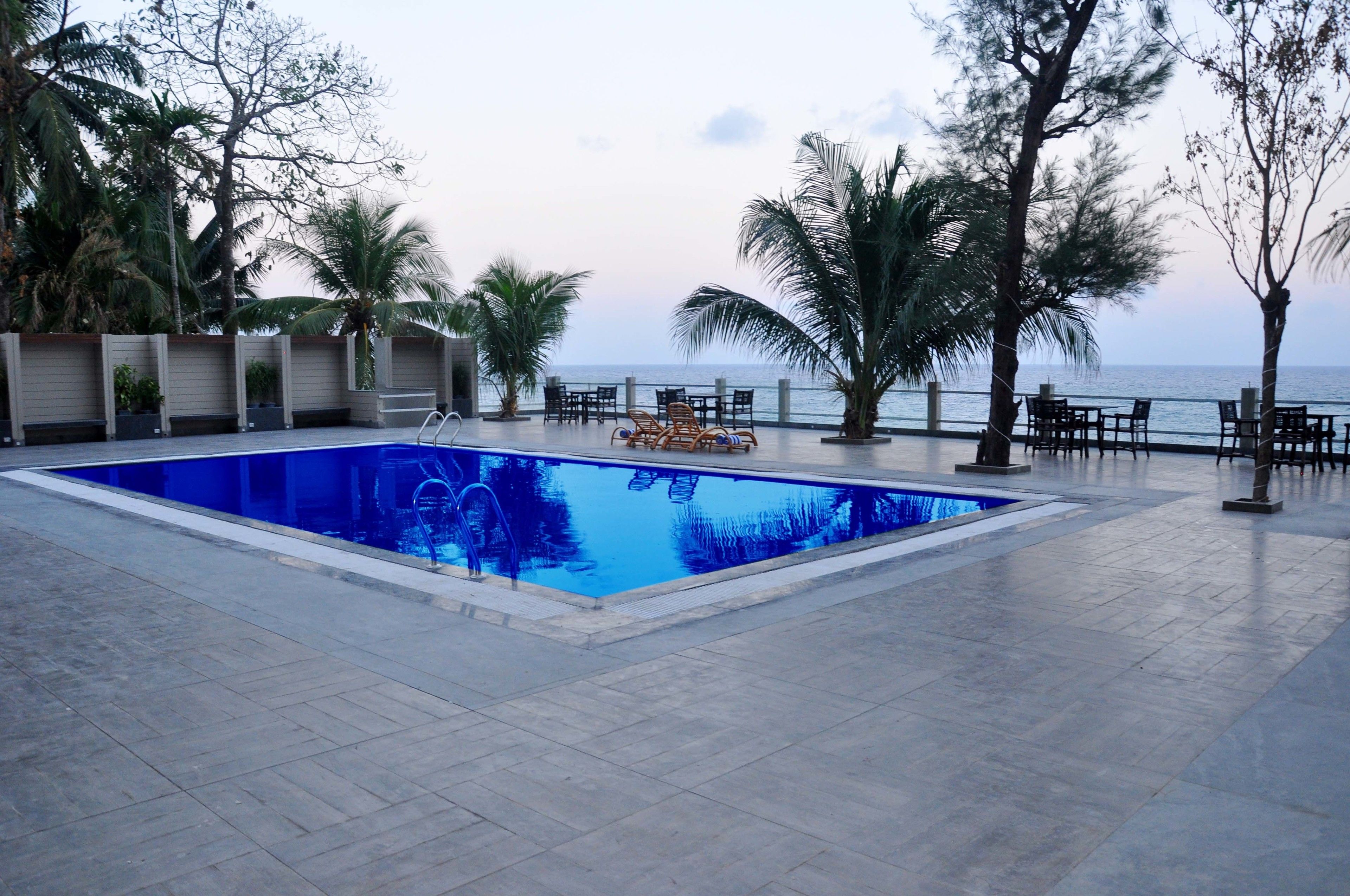 Ein Pool mit Meerblick, umgeben von Palmen und einer Terrasse.