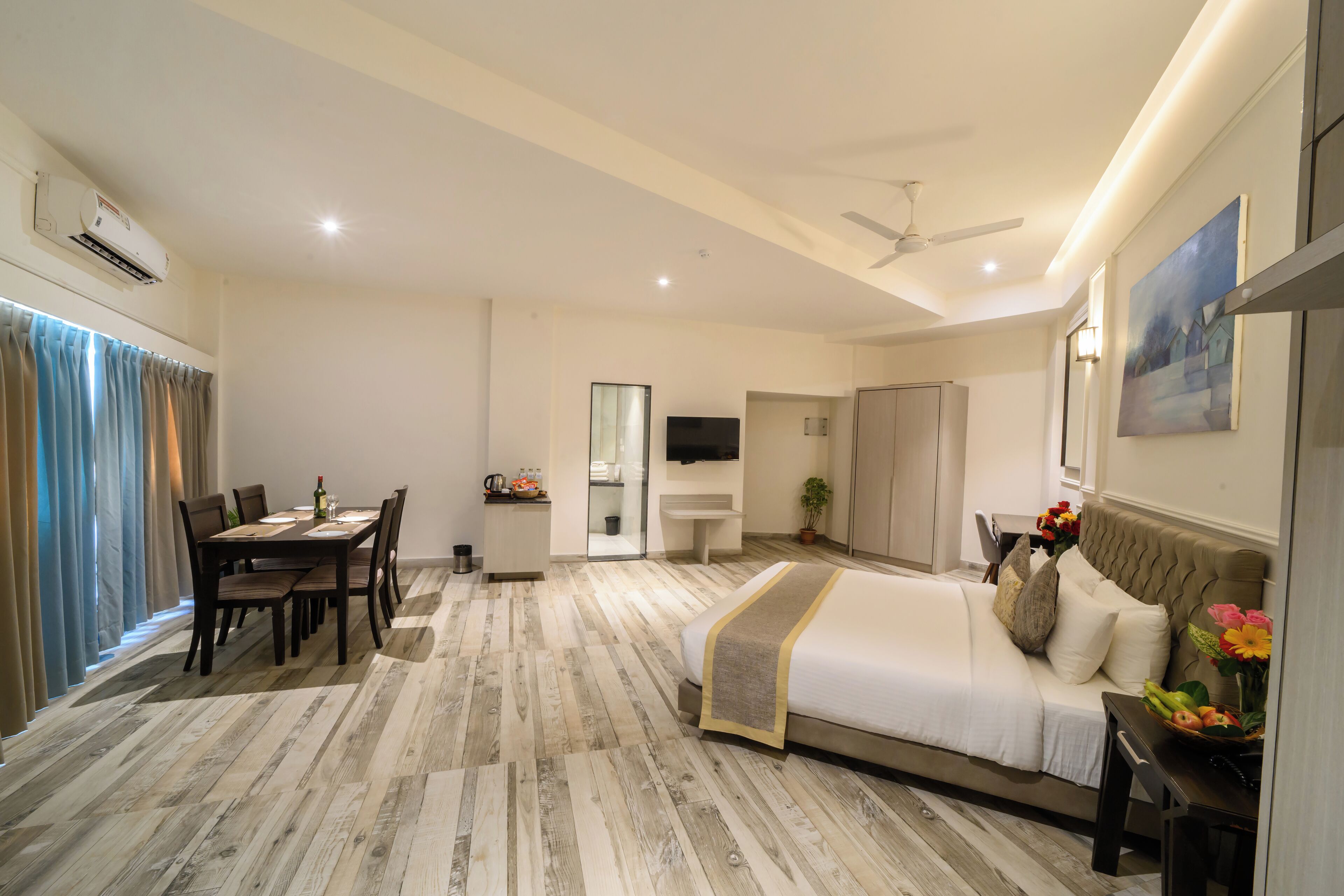 Habitación de hotel con cama, una mesa de comedor con sillas, una pequeña cocina y un baño, además de un ventilador de techo.