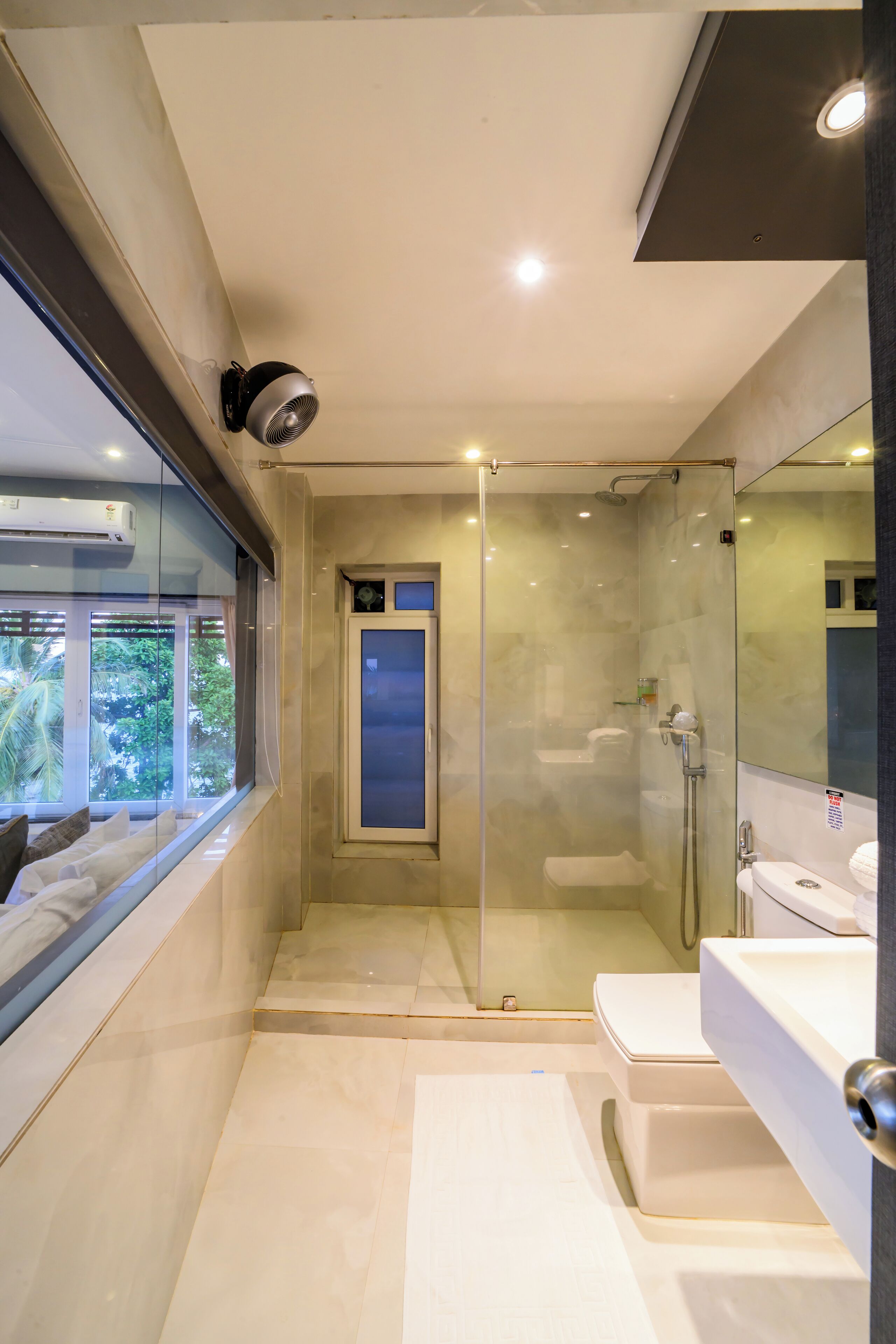 A modern bathroom with a glass-enclosed shower, a large window, and a vanity with a mirror.