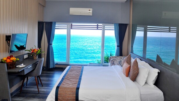 Quarto de hotel com cama, escrivaninha, poltrona, televisão e vista para o oceano.