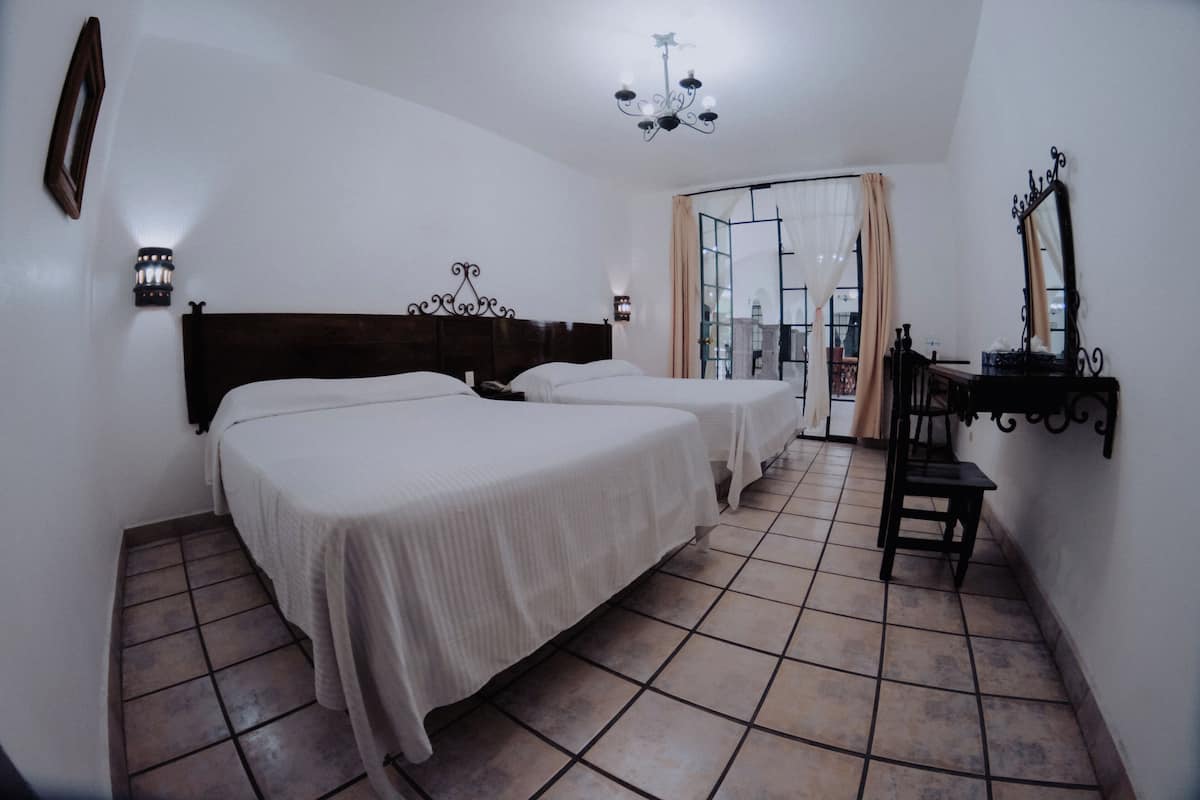 A bedroom with two beds, a wooden headboard, a chandelier, a desk with a chair, and a large window with curtains.