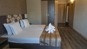 A hotel room with a bed, a wooden bedside table, a wardrobe, and a bathroom visible in the background. - Kotva (Nessebar)