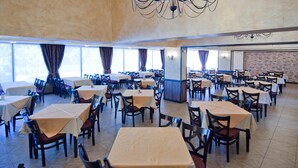 Un comedor amplio con varias mesas y sillas, un candelabro y ventanas grandes que dejan entrar luz natural.