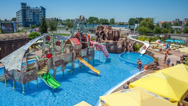 Ein Wasserpark mit Rutschen und Schwimmbecken, umgeben von Gebäuden und Bäumen.
