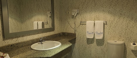 Une salle de bain avec un lavabo doté d’un plan de toilette en granit, un miroir, deux serviettes suspendues à un porte-serviettes et des toilettes.