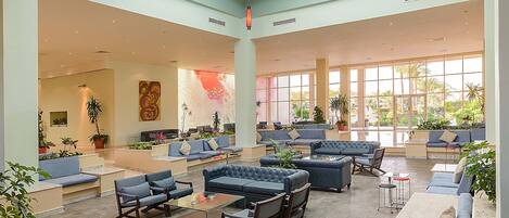 A spacious indoor lobby with multiple seating areas, large windows, and indoor plants.