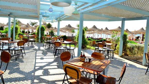 An outdoor dining area with tables and chairs, umbrellas, and a view of the beach. - Prima Life Makadi Hotel - All inclusive (Makadi Bay)
