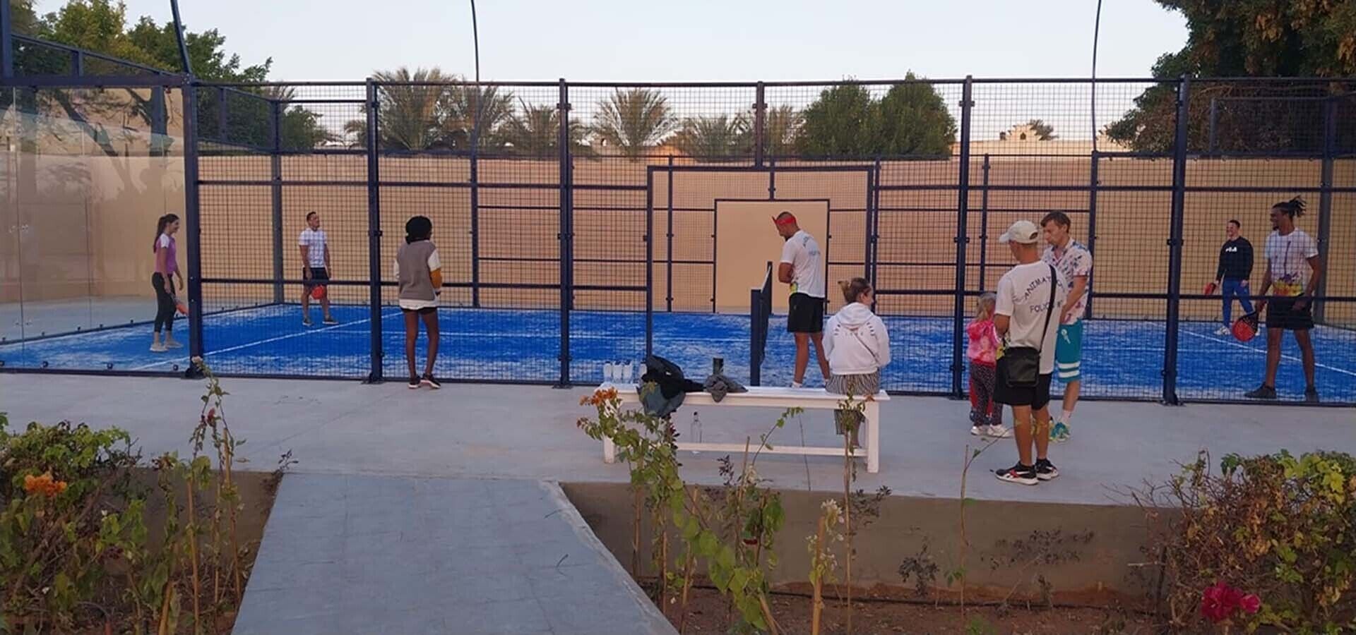 An outdoor tennis court with a net, surrounded by a fence.