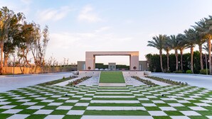 A checkered lawn leading to a building with a central archway, surrounded by palm trees and a clear sky. - Prima Life Makadi Hotel - All inclusive (Makadi Bay)