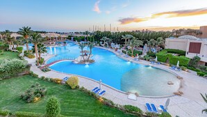 A large swimming pool with multiple sections, surrounded by palm trees and lounge chairs. - Prima Life Makadi Hotel - All inclusive (Makadi Bay)