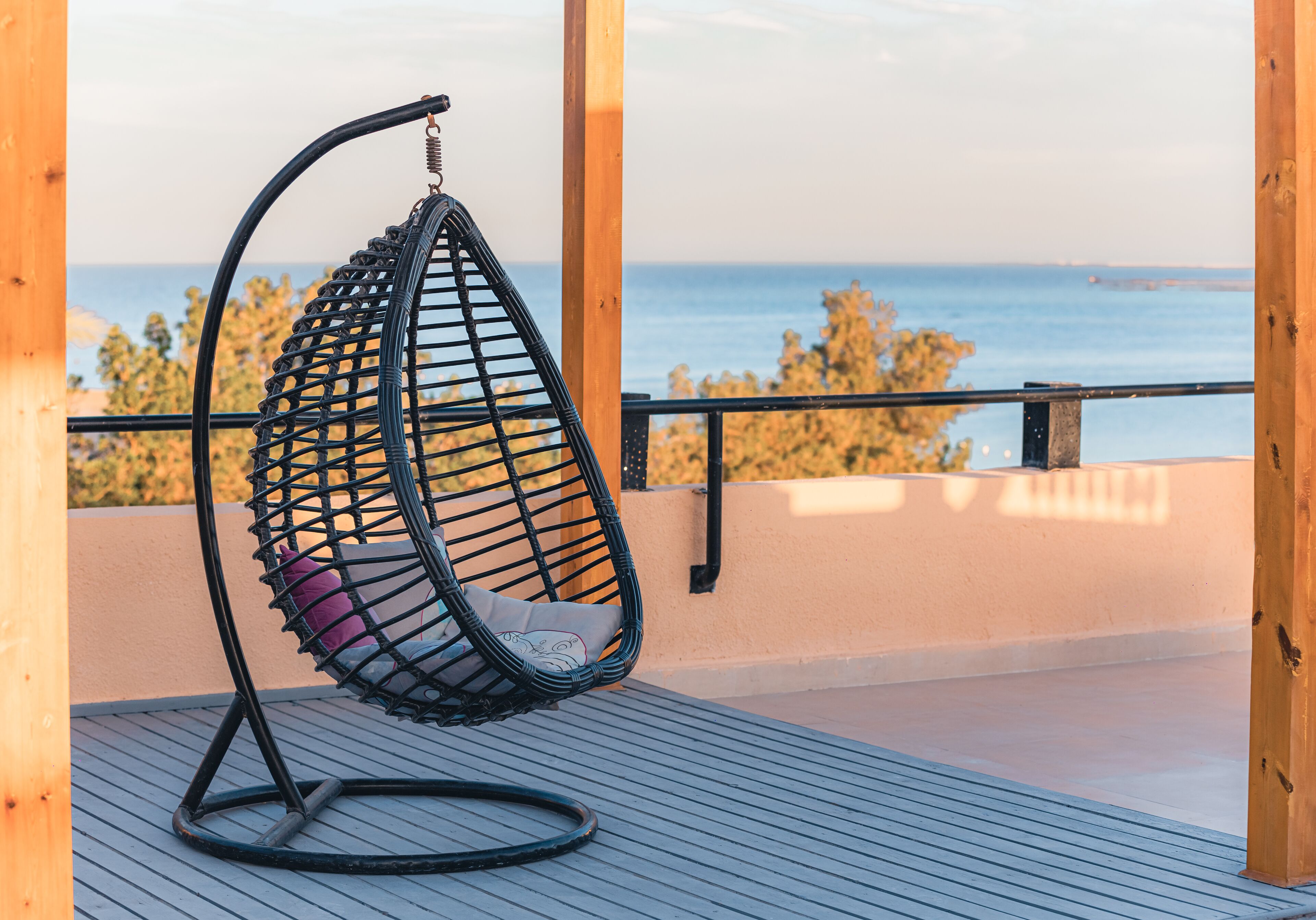 Een zwarte hangstoel met kussen op een houten terras, met uitzicht op zee.