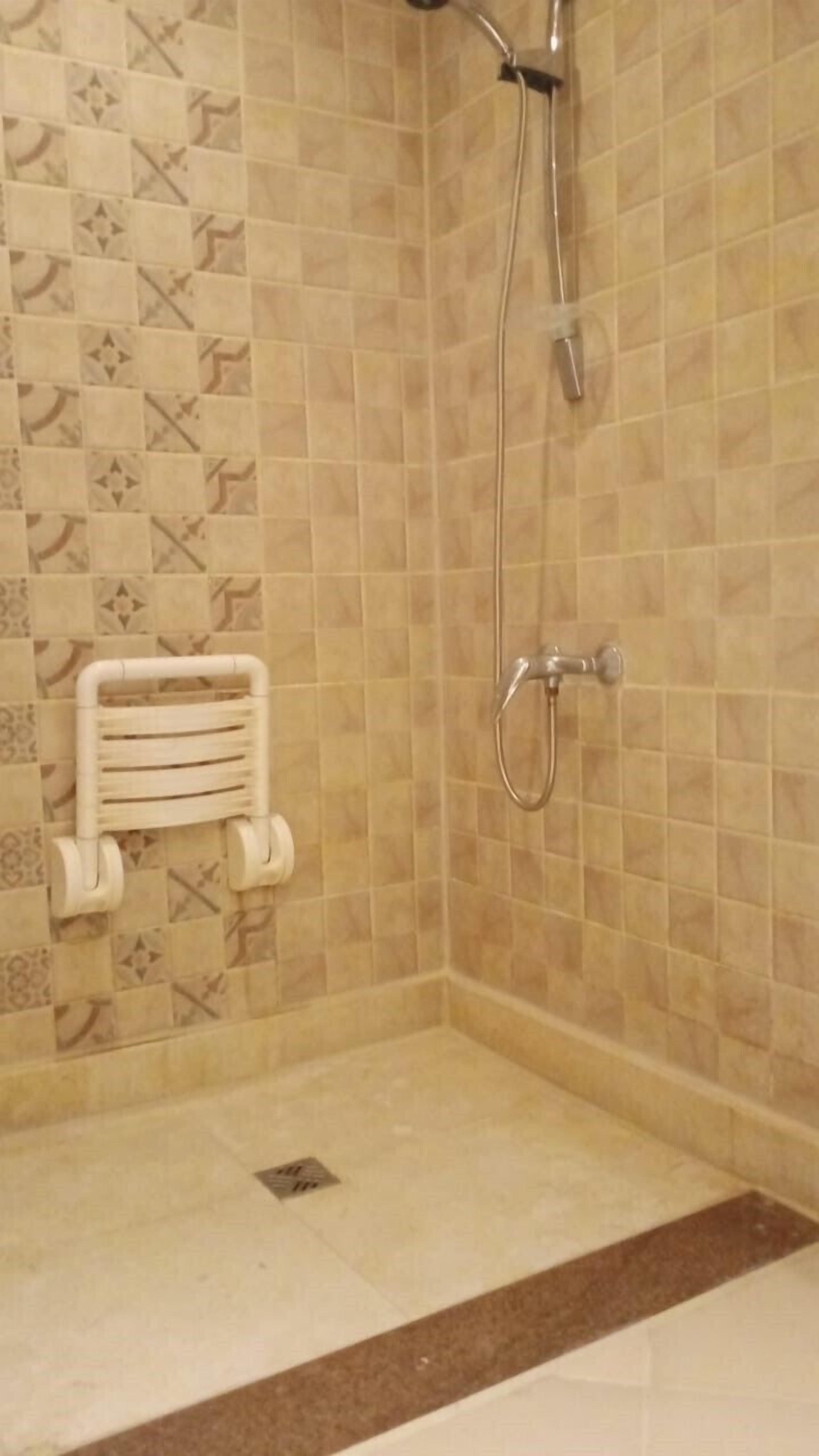 A shower area with tiled walls and a floor, a towel rack, and a showerhead.