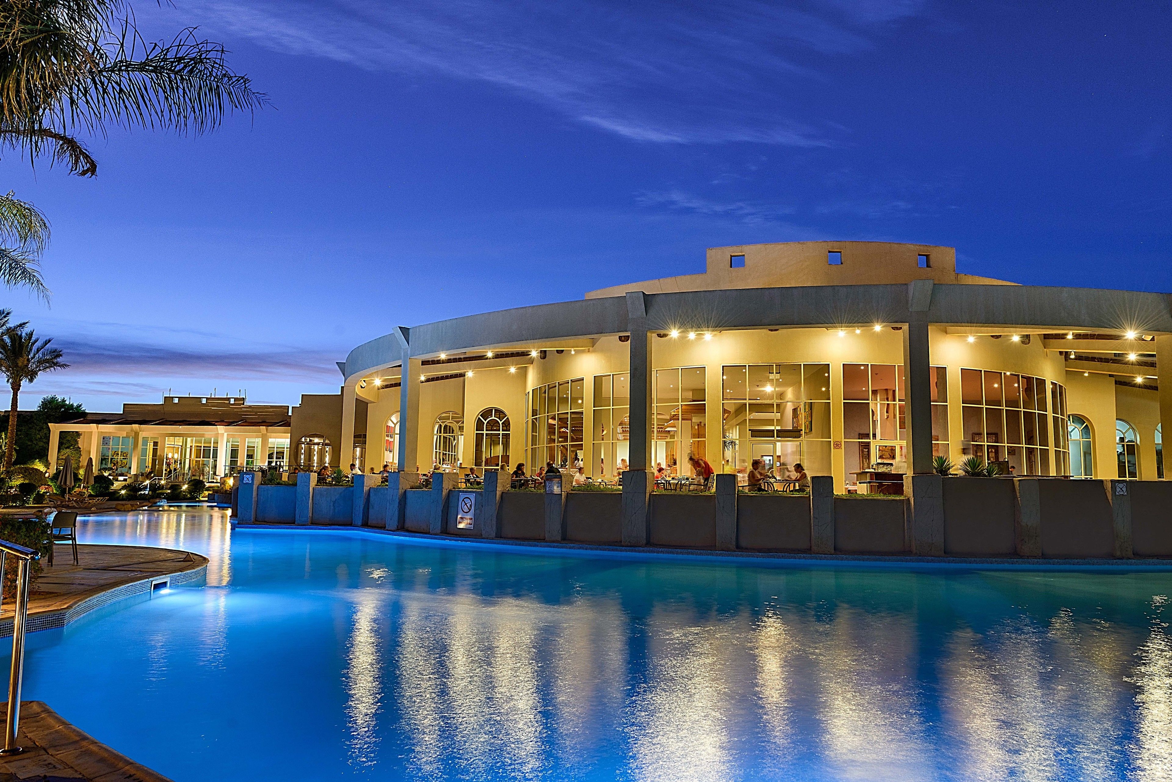 A hotel with a pool, outdoor seating, and a large building with multiple windows.